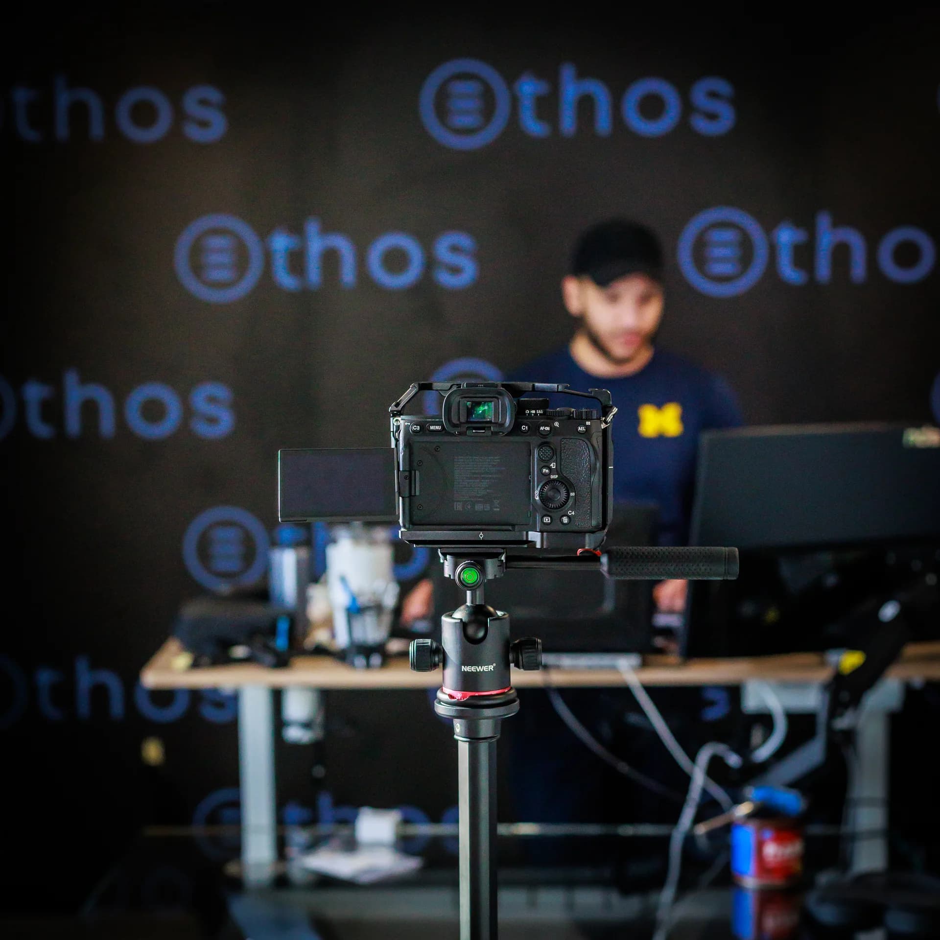 Camera on a tripod filming a session in front of an Ethos backdrop